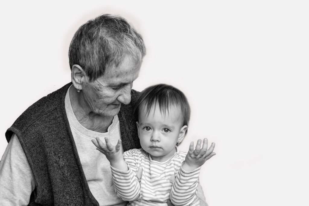 "luto vó", "luto vô", "luto avós". imagem ilustra texto sobre luto pelos avós. uma mulher idosa aparece à esquerda segurando uma criança pequena no colo. a imagem é em preto e branco.
