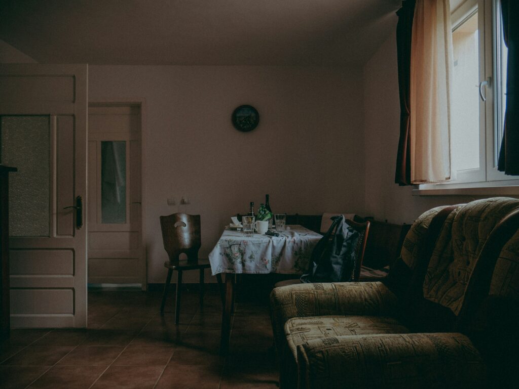 foto ilustra texto "Morte em Casa: O Que Fazer em Casos de Falecimento Domiciliar". uma sala de estar vazia. sofá vazio e pequena mesa de jantar vazia com copos e garrafas usados. 