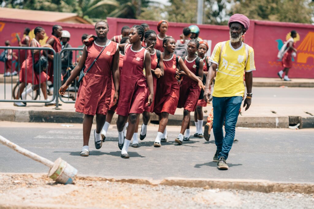 a vida após a morte no rastafrianismo. homem rastafari aparece em primeiro plano usando turbante, calça jeans e camiseta retrô de futebol. ao fundo, meninas adolescentes na saída da escola